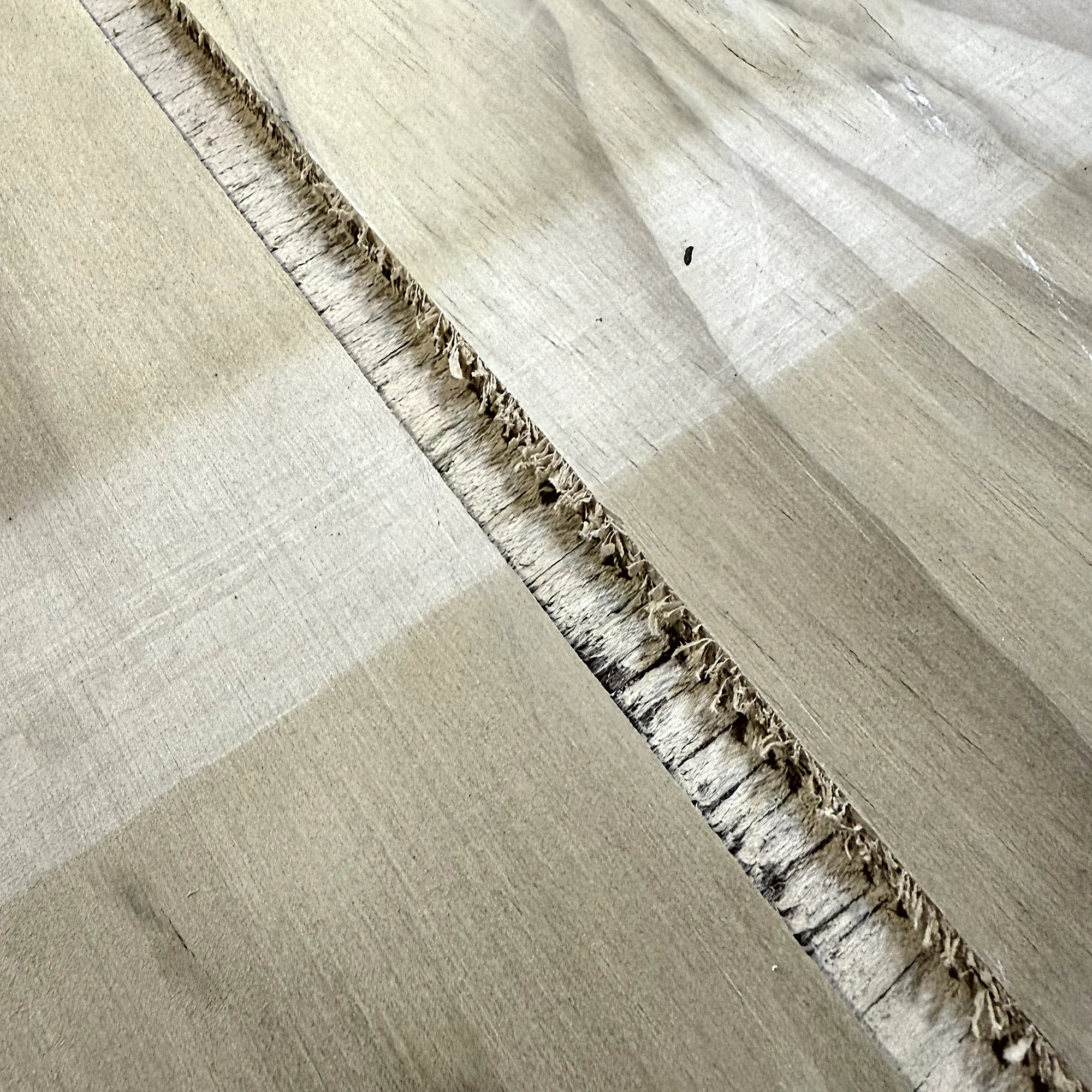 Close-up of light pine plywood sheet showing a rough, frayed U-grooved cut along its length.